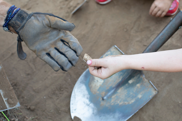 A young volunteer hands an artifact to the project PI